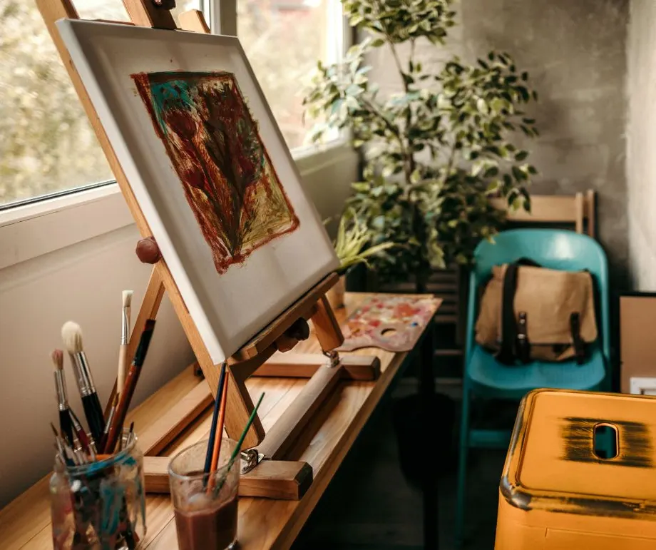 Framed artwork on an easel beside brushes and paints